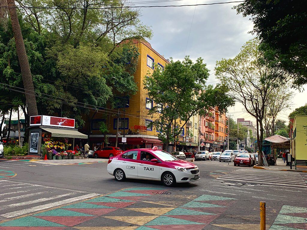 a pink and white CDMX taxi drives through an intersection in La Condesa, Mexico City