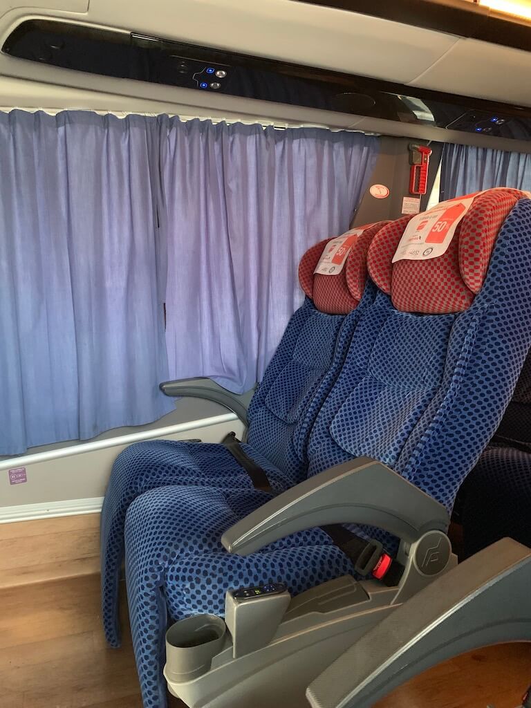 Interior view of an ADO bus in Mexico showing spacious seats with blue patterned fabric and individual controls and amenities for a comfortable ride.