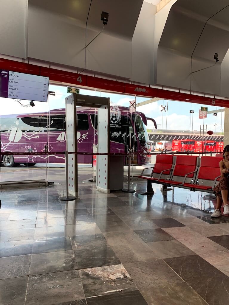 rows of empty chairs in front of a plate glass window in the ADO Platino and GL lounge in TAPO Bus Station, Mexico City. ADO GL bus is seen through the window. 