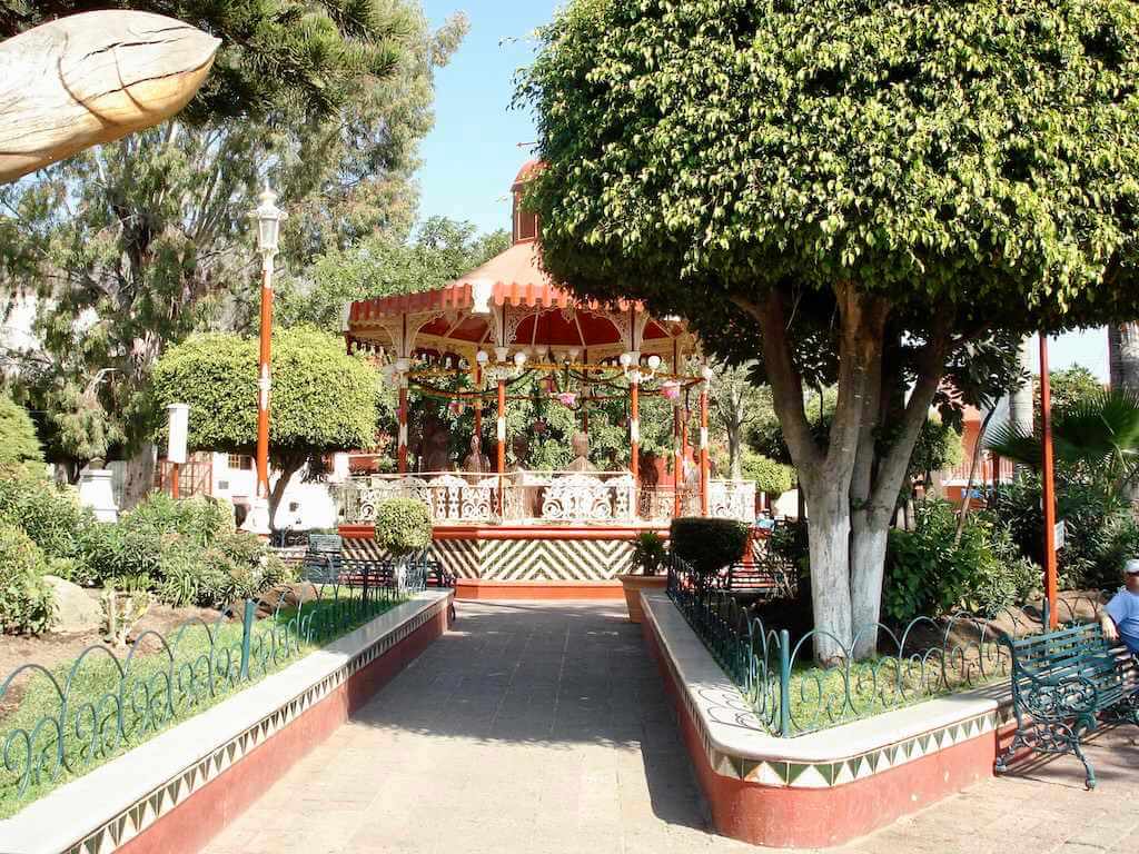 view of the gazebo in the main square of Ajijic, Mexico with lush plants and park benches in the foreground