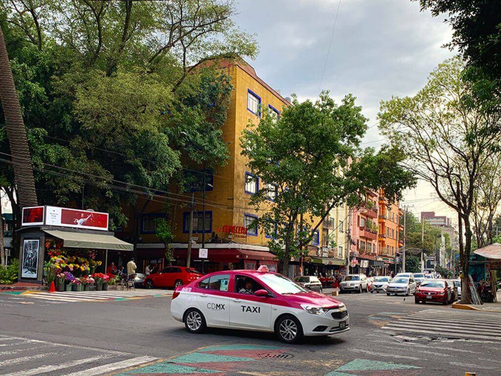 pink and white taxi crossing through a colorful intersection in Mexico City