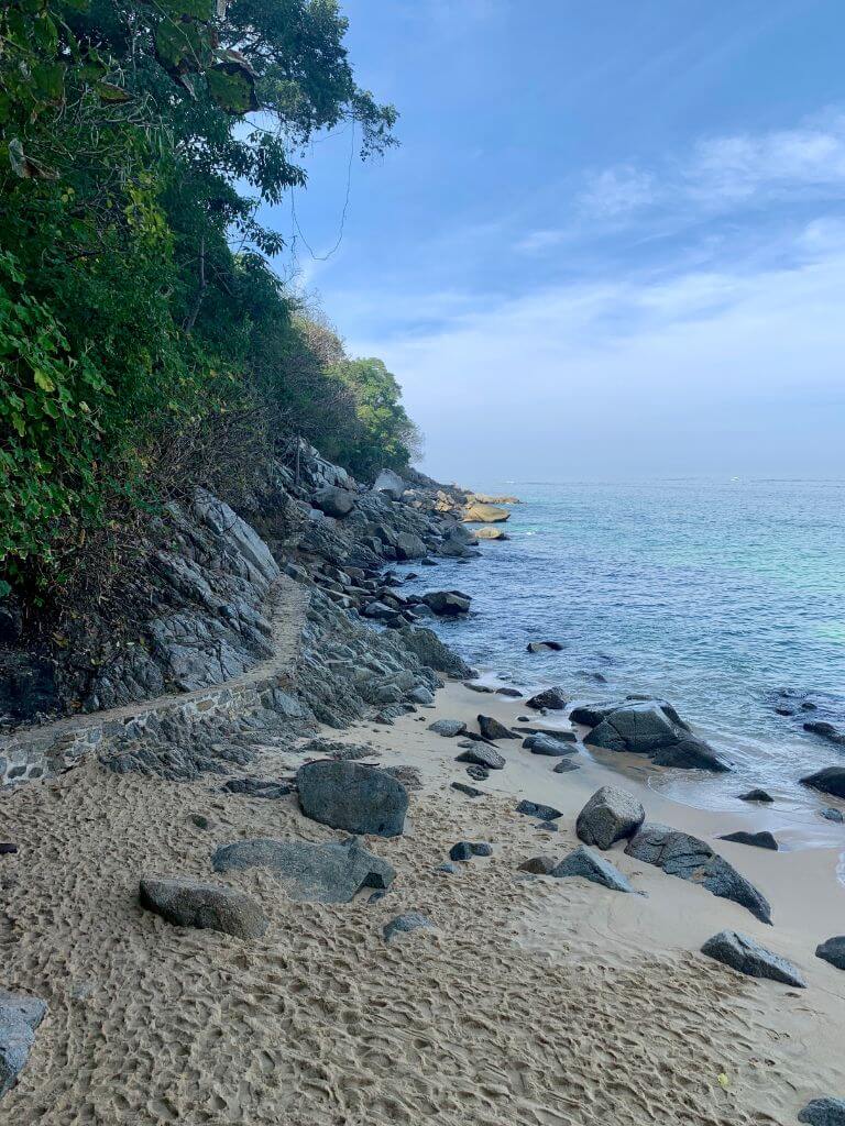 A narrow concrete path follows the shoreline toward Playa Las Animas as you leave Playa Colomitos