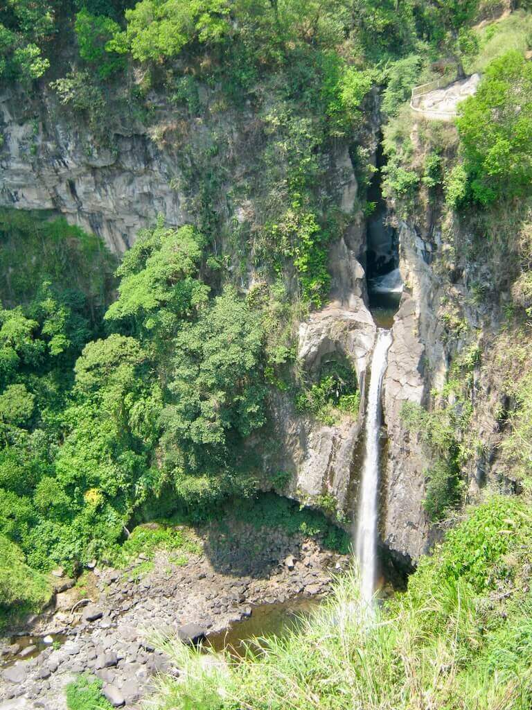 Cascada Texolo waterfall pours from cliffside pools into a rocky pool below. Green trees and plants grow out of the rocky cliffs surrounding the falls