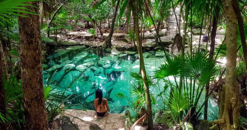 woman sits on the edge of a turquoise-green cenote