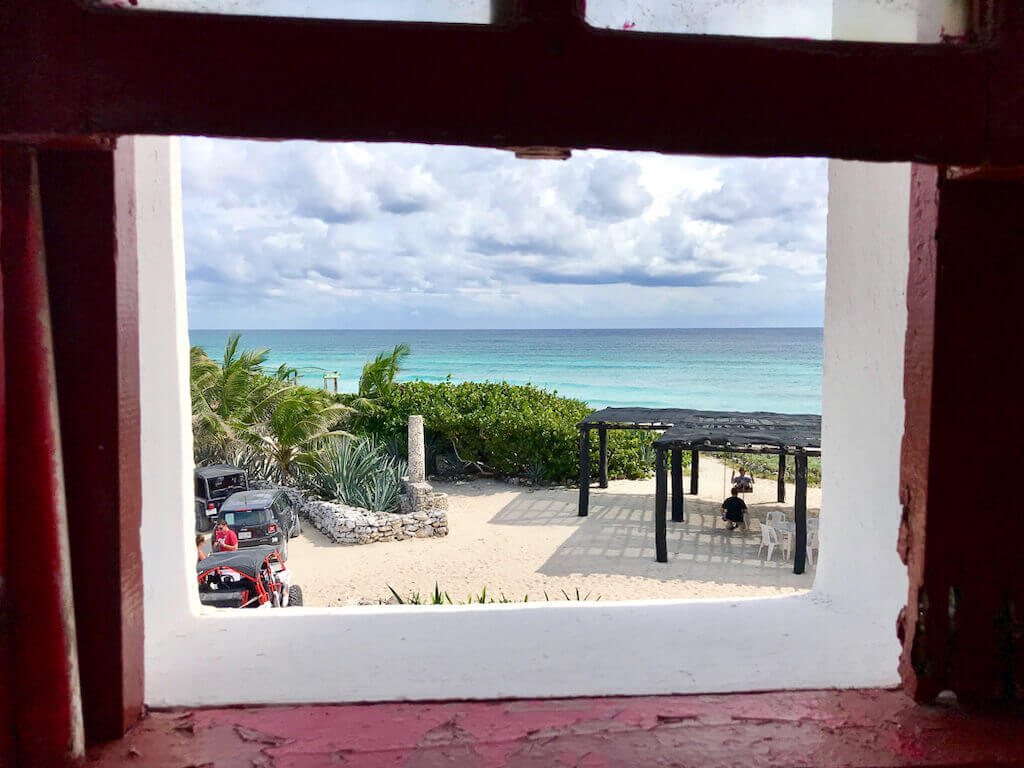 A shot looking out the window of the Punta Sur lighthouse on Cozumel with the sandy beach and blue ocean in the distance.