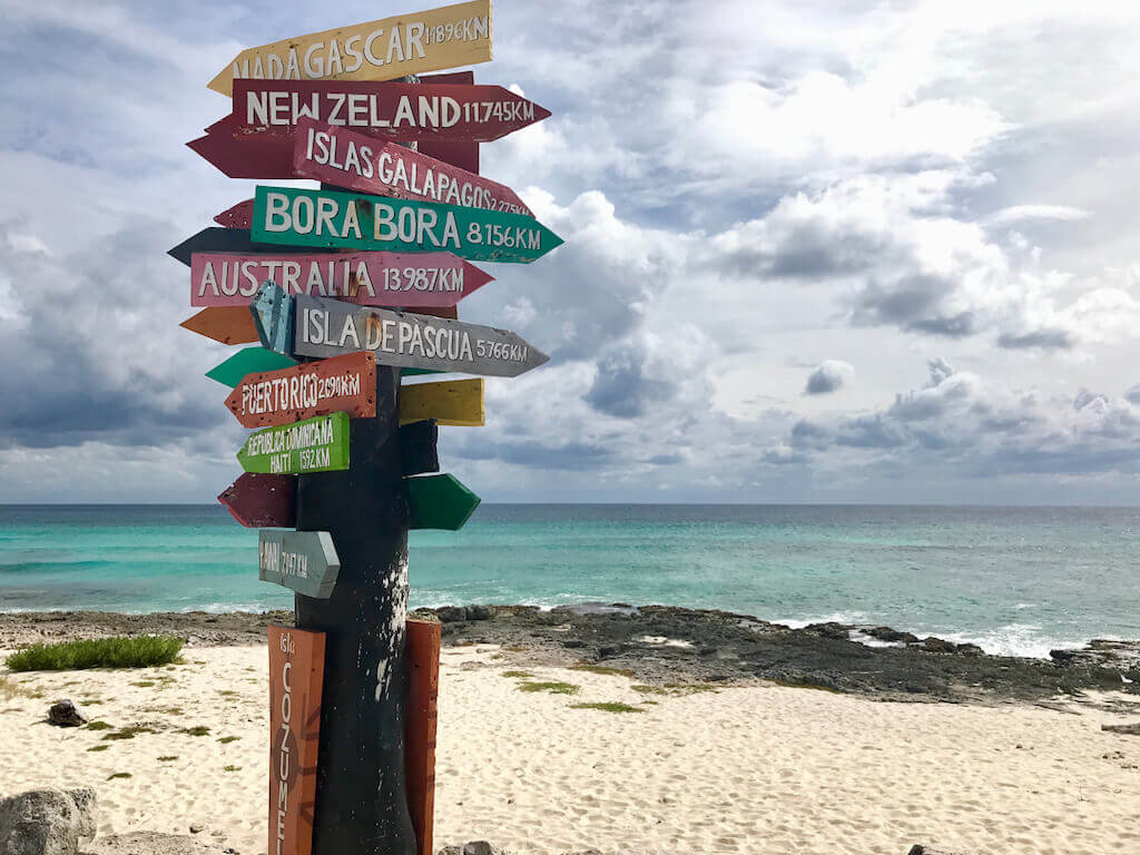 Colorful directional sign post at Cozumel's Punta Sur lighthouse with the Caribbean sea in the background