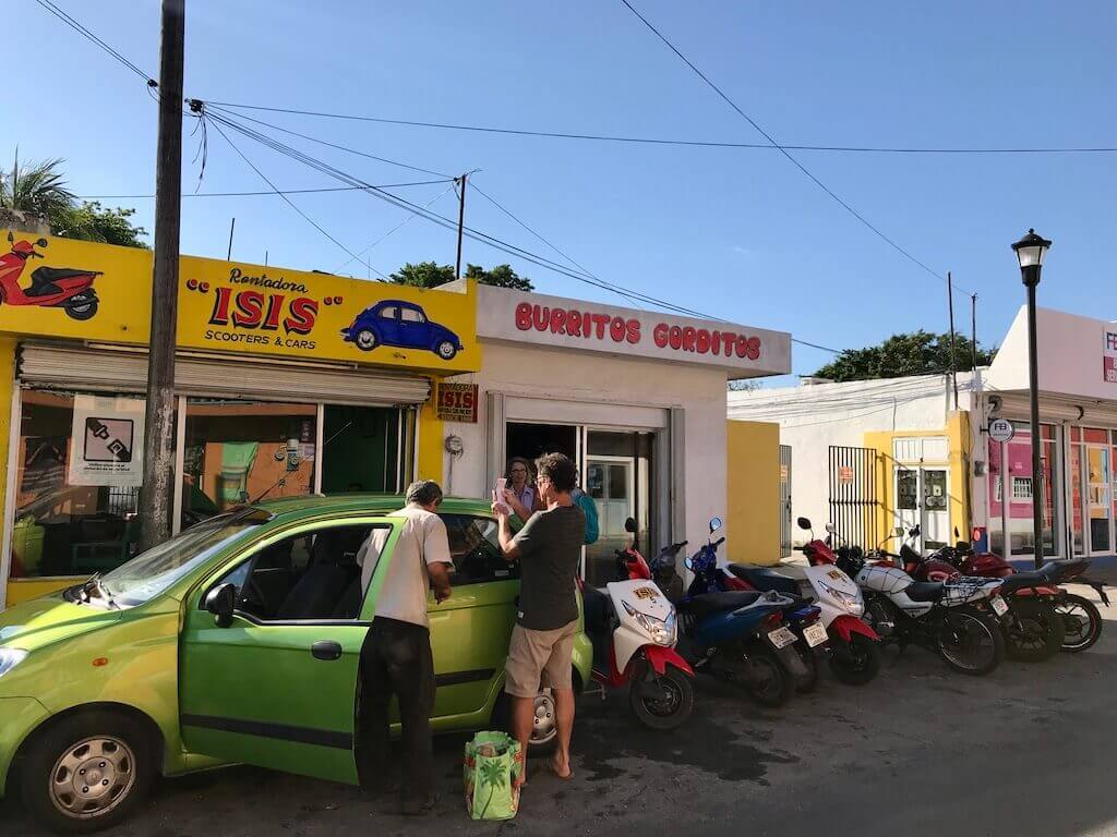 my dad discusses the terms of the rental car agreement in front of a lime green hatchback car, with the car rental shop in the background