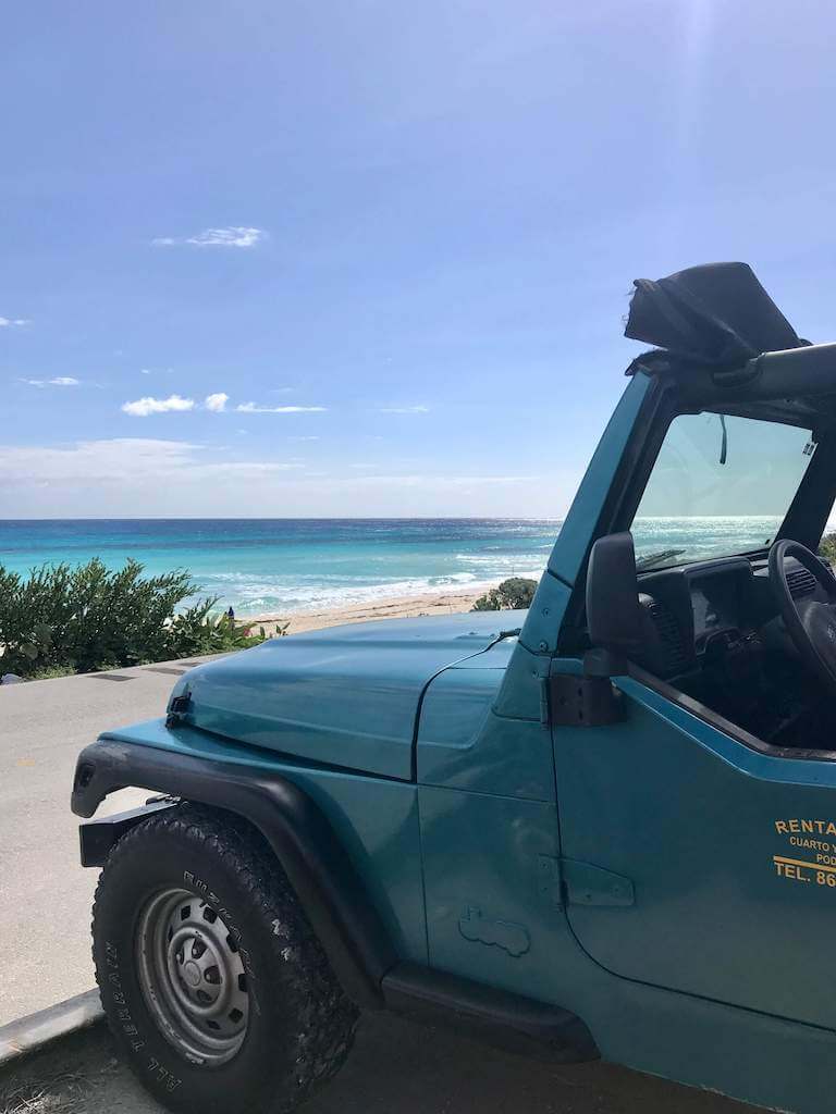 turquoise jeep parked in front of the turquoise ocean on Cozumel Island