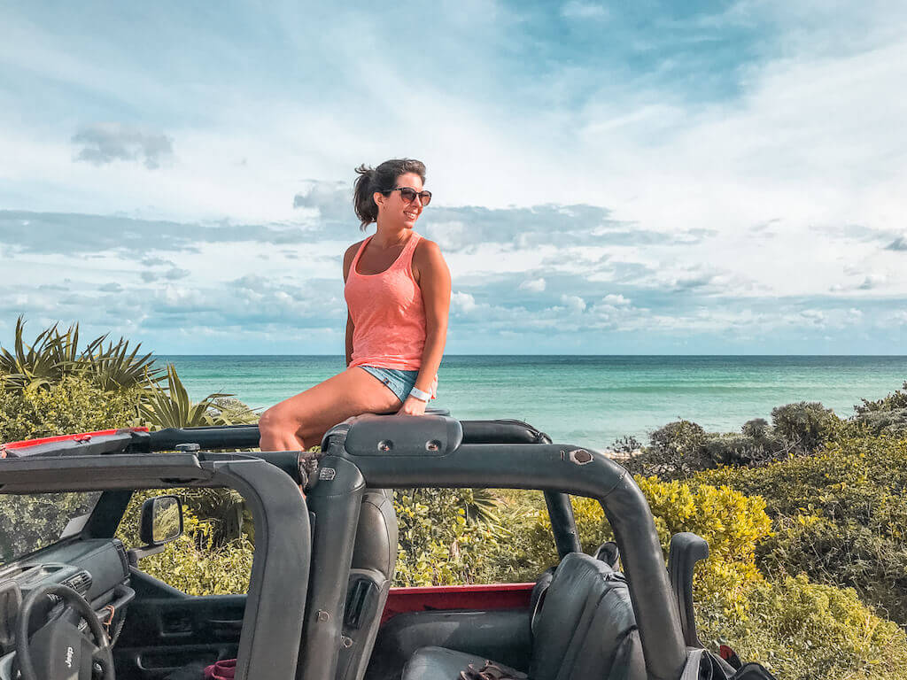 Janine perched on top of a jeep on Cozumel with the cerulean Caribbean sea in the background