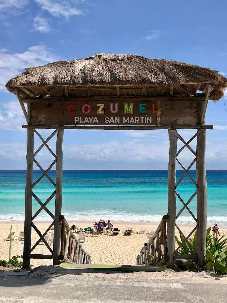 A thatched archway reading "Playa San Martin" frames the Caribbean Sea in the distance on Cozumel Island