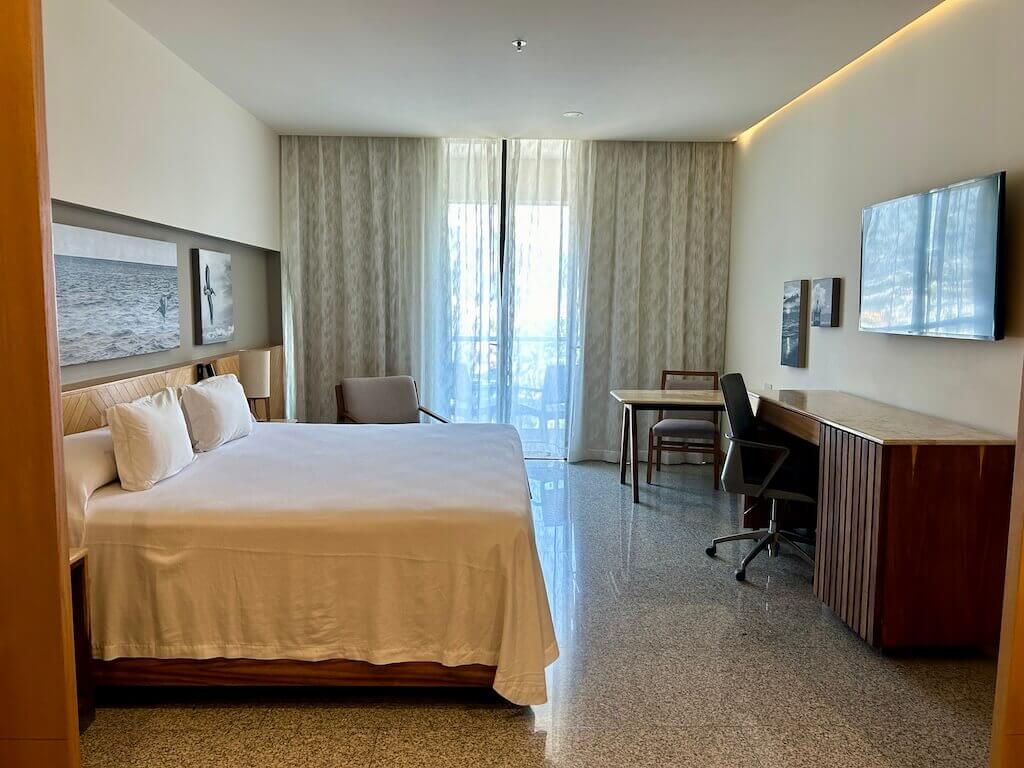 looking into a king room at the hotel Mio Vallarta, king bed on the left with a desk and table on the right and doors leading to the balcony straight ahead