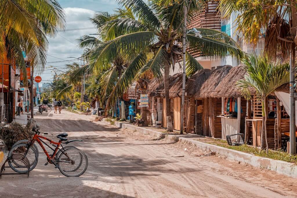 unpaved street lined with palm trees and palapa roofs in Isla Holbox, Mexico