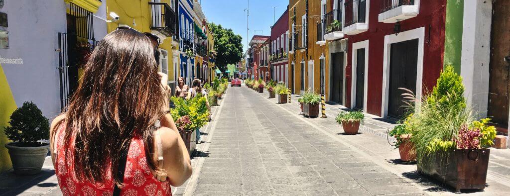 looking over the shoulder of a solo female traveler taking a photo of the colorful calle de los sapos in Puebla, Mexico