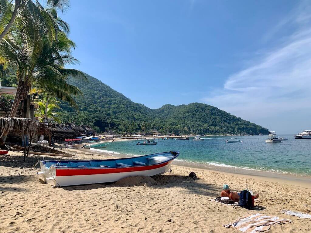 a white panga boat with a red stripe rests on the sandy Las Animas beach with a bay full of boats in the distance