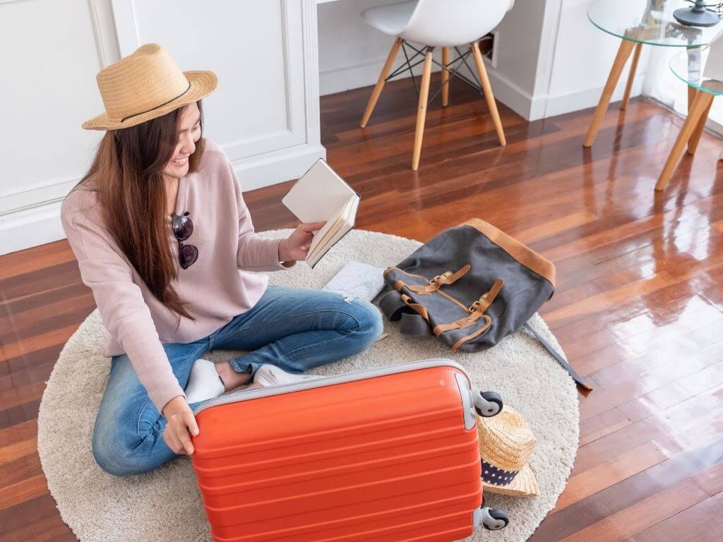 female traveler sitting on the floor packing a red hard-sided suitcase