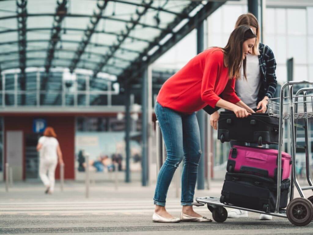 women load suitcases onto a luggage cart in a bus station