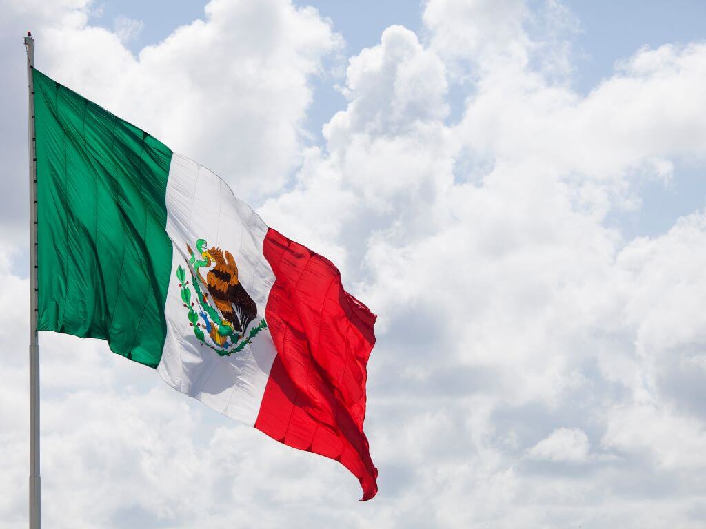 close shot of the mexican flag blowing in the wind with clouds in the background