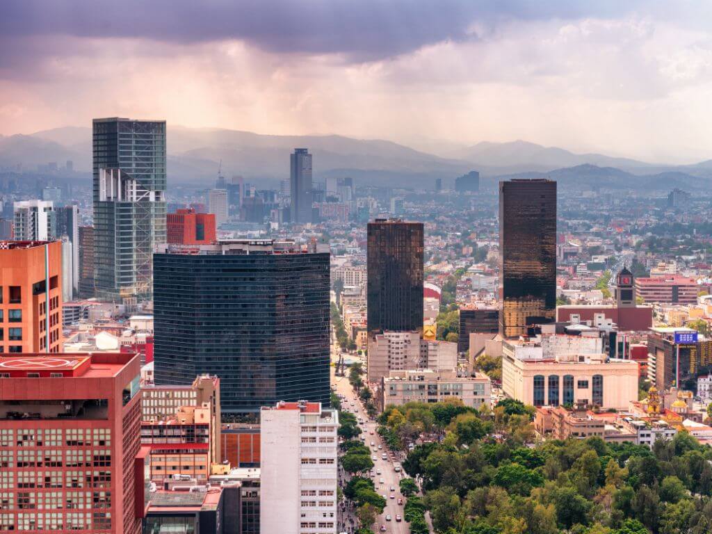 Panoramic view of Mexico City's skyline with a variety of modern skyscrapers against a backdrop of distant mountains and overcast skies, highlighting the vast urban landscape at high altitude, in which some travelers struggle with altitude sickness.