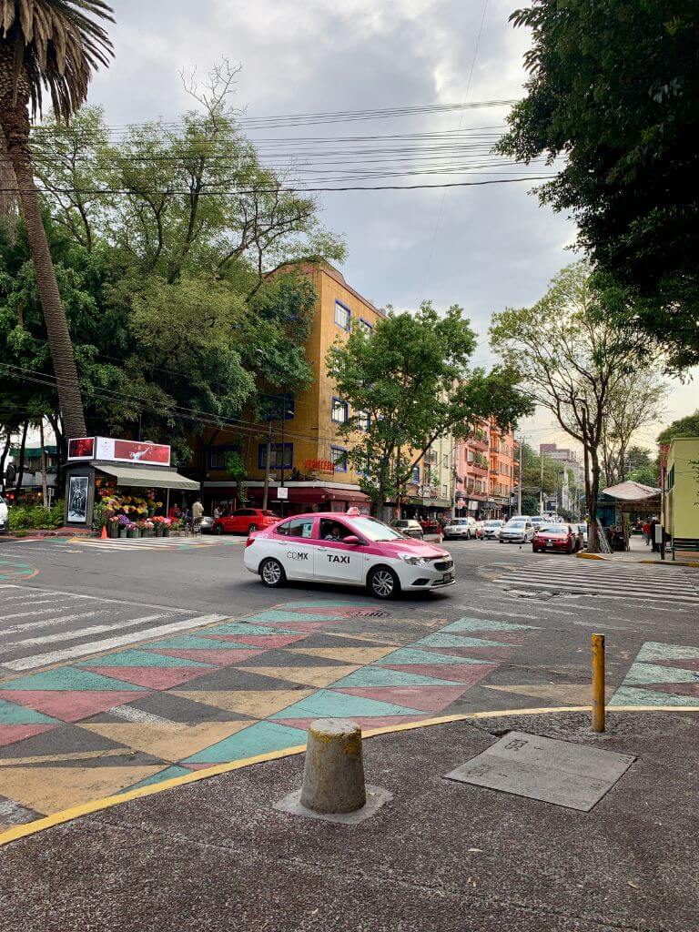 a pink and white taxi drives through an intersection with colorful crosswalks in the Condesa neighborhood of Mexico City