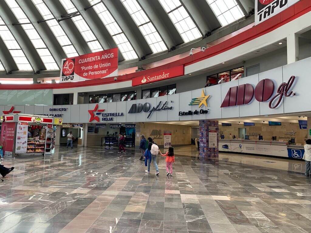 The bustling interior of TAPO bus terminal in Mexico City, showcasing various bus ticket counters including ADO.