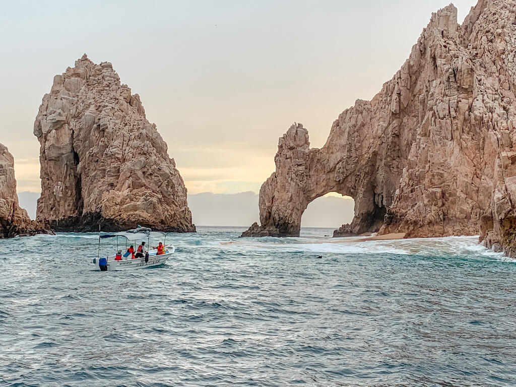 the arches rock formation in cabo san lucas, mexico with a panga boat carrying 4 passengers in the foreground