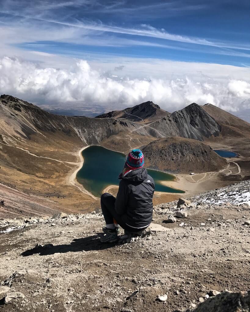 Woman crouched on a barren mountain overlooking a lake in Mexico, called Nevado de Toluca