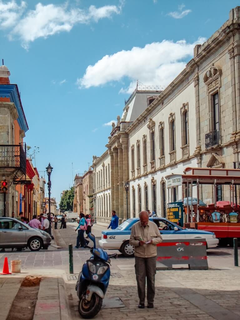 a man writes a note next to a scooter on a cobblestone street in Oaxaca, Mexico with traffic passing in the background