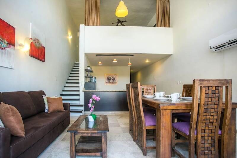 living area of an airbnb with dining table on the right and couch to the left with stairs leading to loft in the background