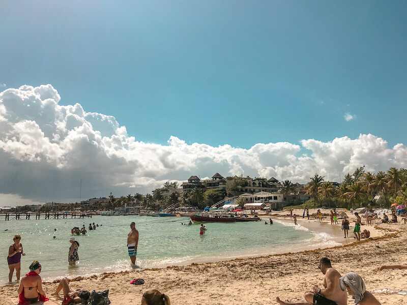 travelers sun tan on Mamitas Beach in Playa del Carmen, with panga boats and palm trees in the distance