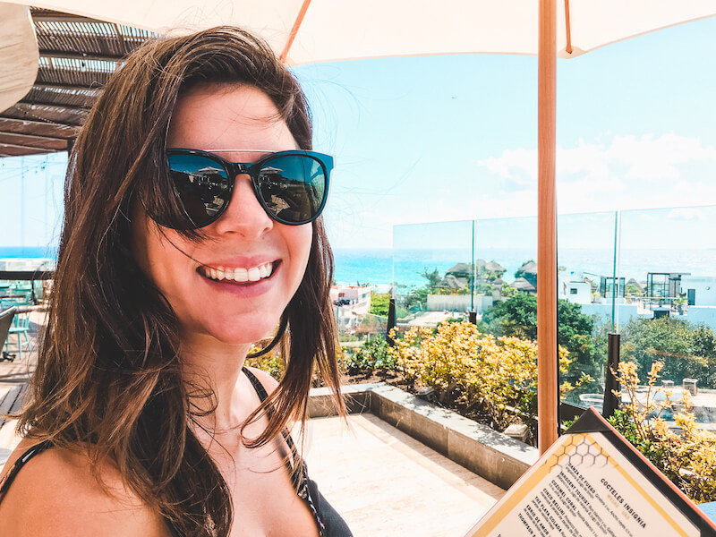 a smiling woman on the rooftop patio at Catch in Playa del Carmen with the Caribbean sea in the distance