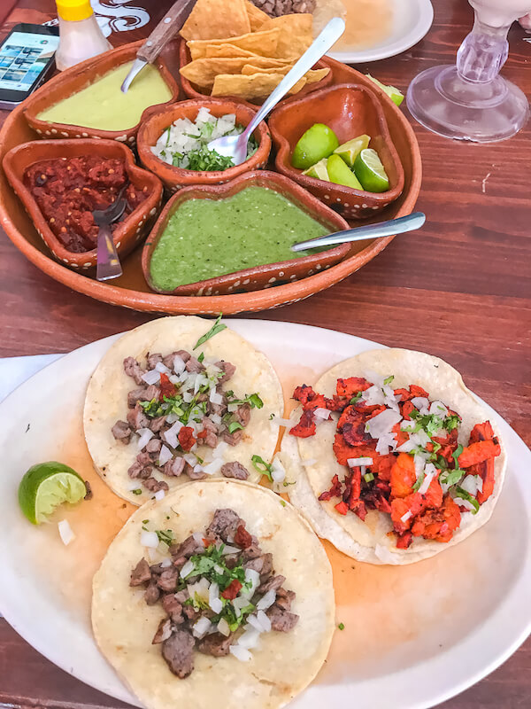 flatlay shot of a plate of steak and pastor tacos and a platter with several different types of salsa and toppings