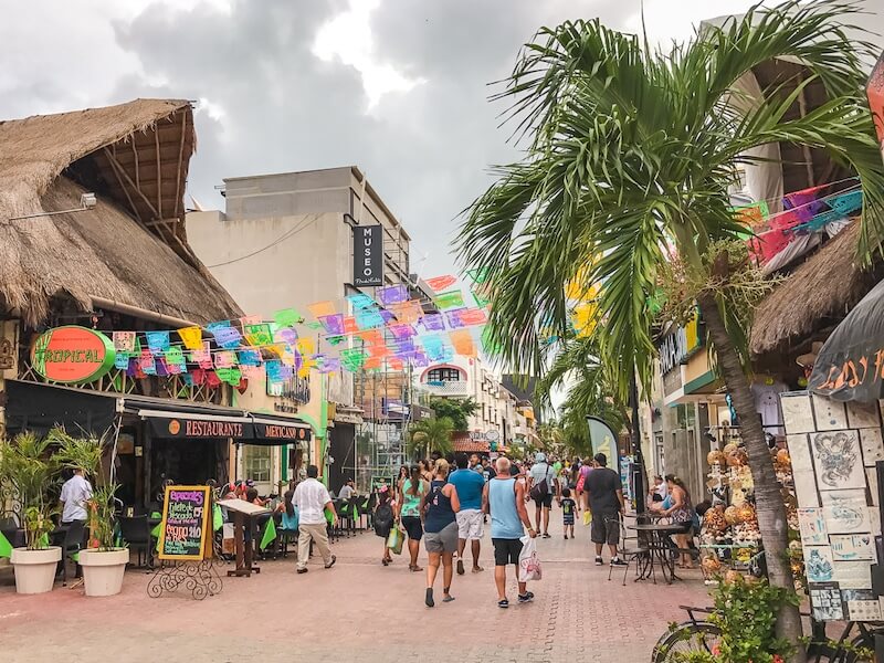 visitors stroll along La Quinta Avenida, a bustling shopping street in Playa del Carmen with papel picado strung overhead