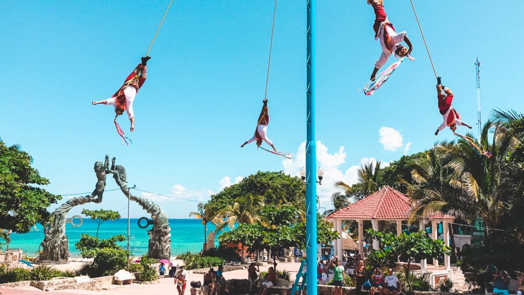 voladores de papantla swing upside down from a pole with the playa del carmen arches and the Carribbean sea in the background