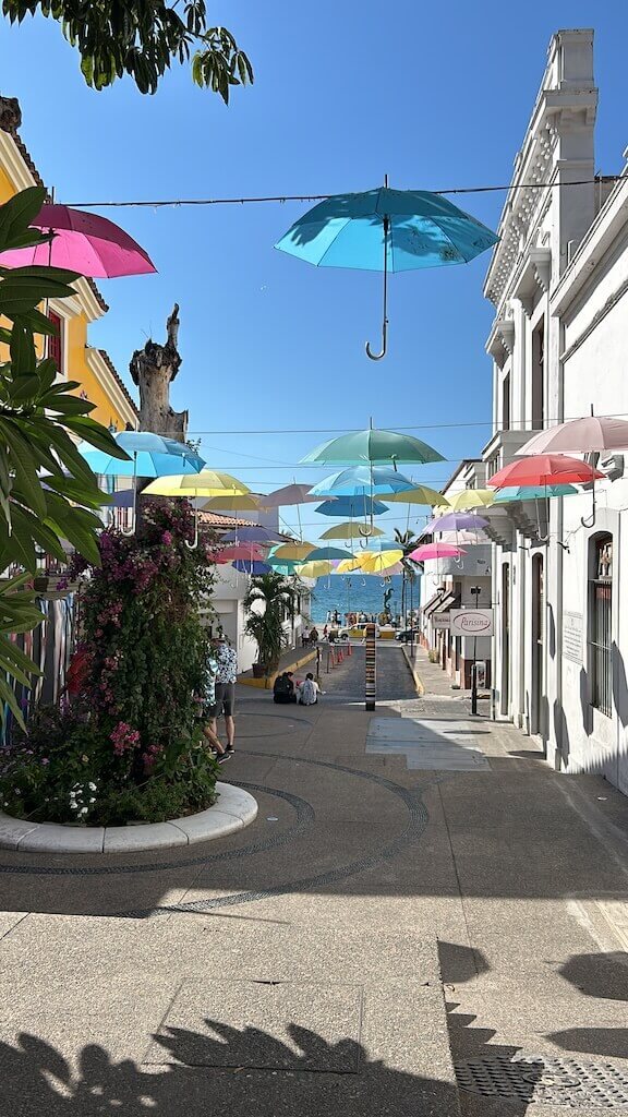 colorful umbrellas are strung up above a pedestrian street leading to the oceanfront boardwalk in Puerto Vallarta, Mexico 