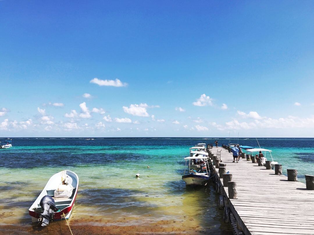 a wooden pier with boats tied up along it extends from the shore in Puerto Morelos, Mexico