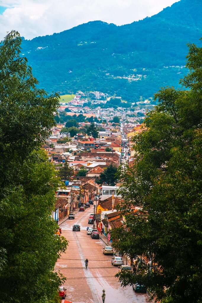 a view down a steep street descending into the center of San Cristobal de las Casas, with green jungle on the hills in the distance