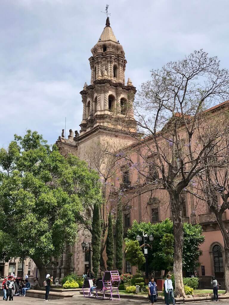 cathedral in san luis potosi with trees in front and people taking pictures in the foreground