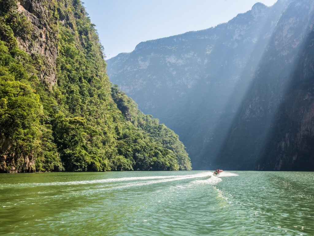 A boat full of tourists motors down the center of the Grijalva River in Sumidero Canyon, one of the best biggest attractions in Chiapas, Mexico