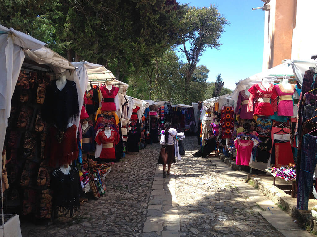 an indigenous woman walks through a market selling textiles in San Cristobal de las Casas, Chiapas