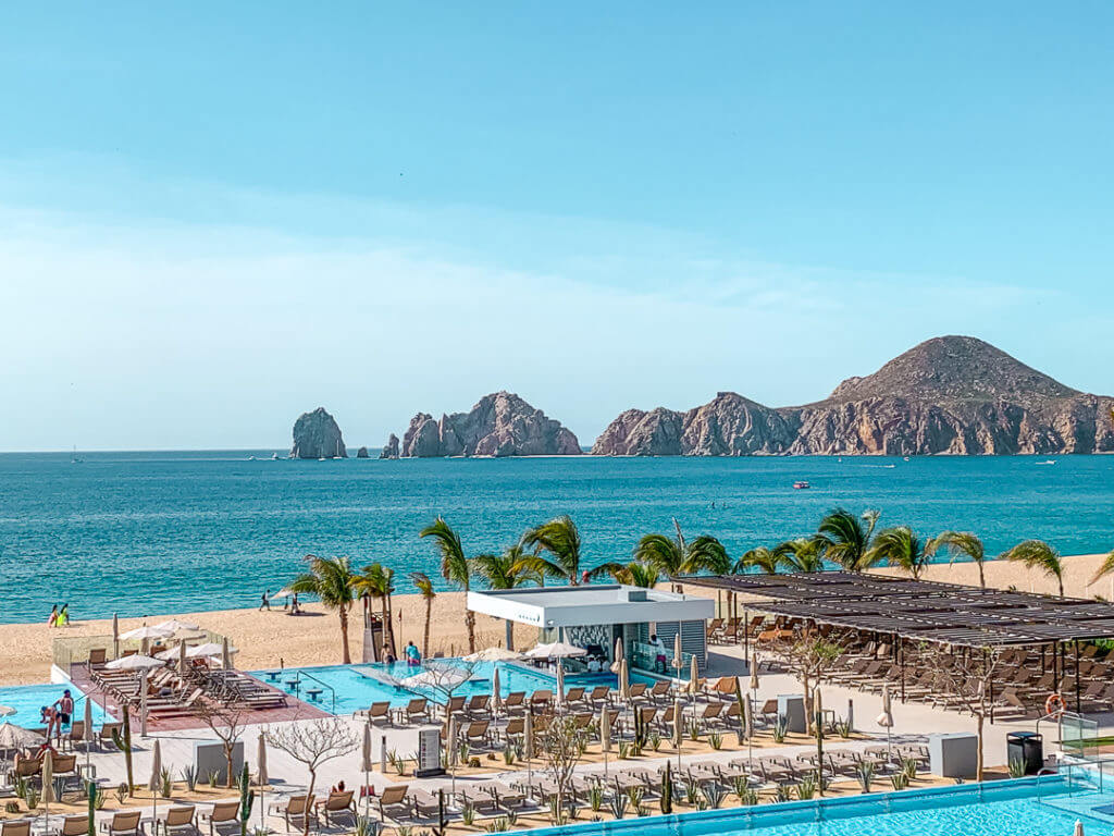 View of a pool at an all inclusive resort in Los Cabos, Mexico with the famous Los Arcos across the bay in the distance