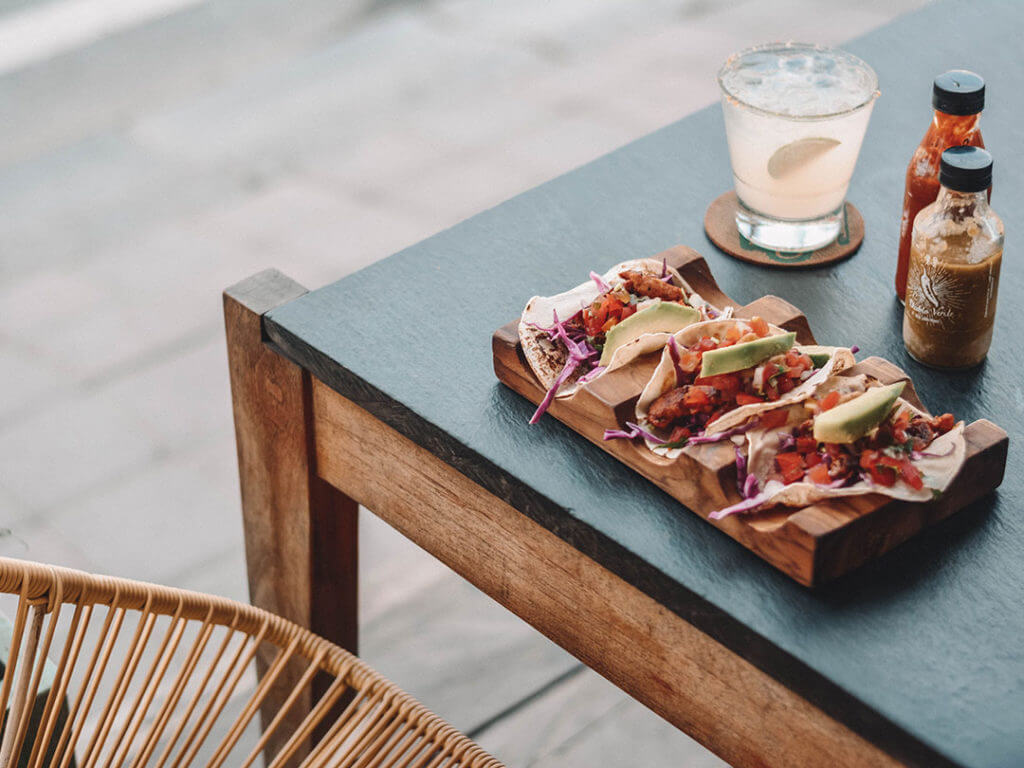 tacos on a table at a restaurant in mexico with two bottles of hot sauce and a margarita