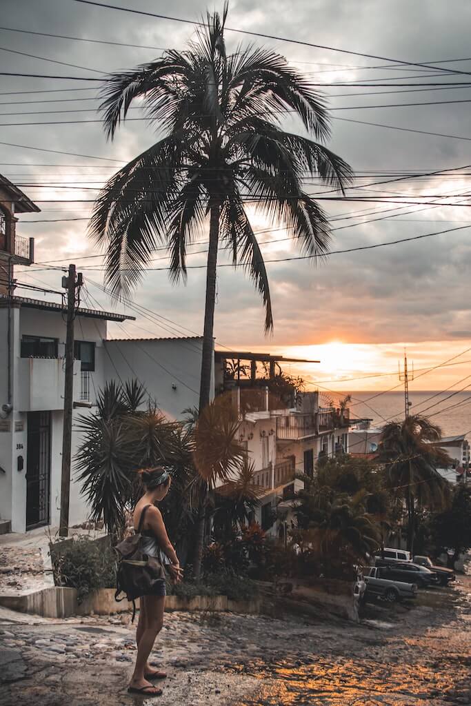 solo female traveler in Mexico walking down a cobblestone street toward the beach with the ocean in the distance