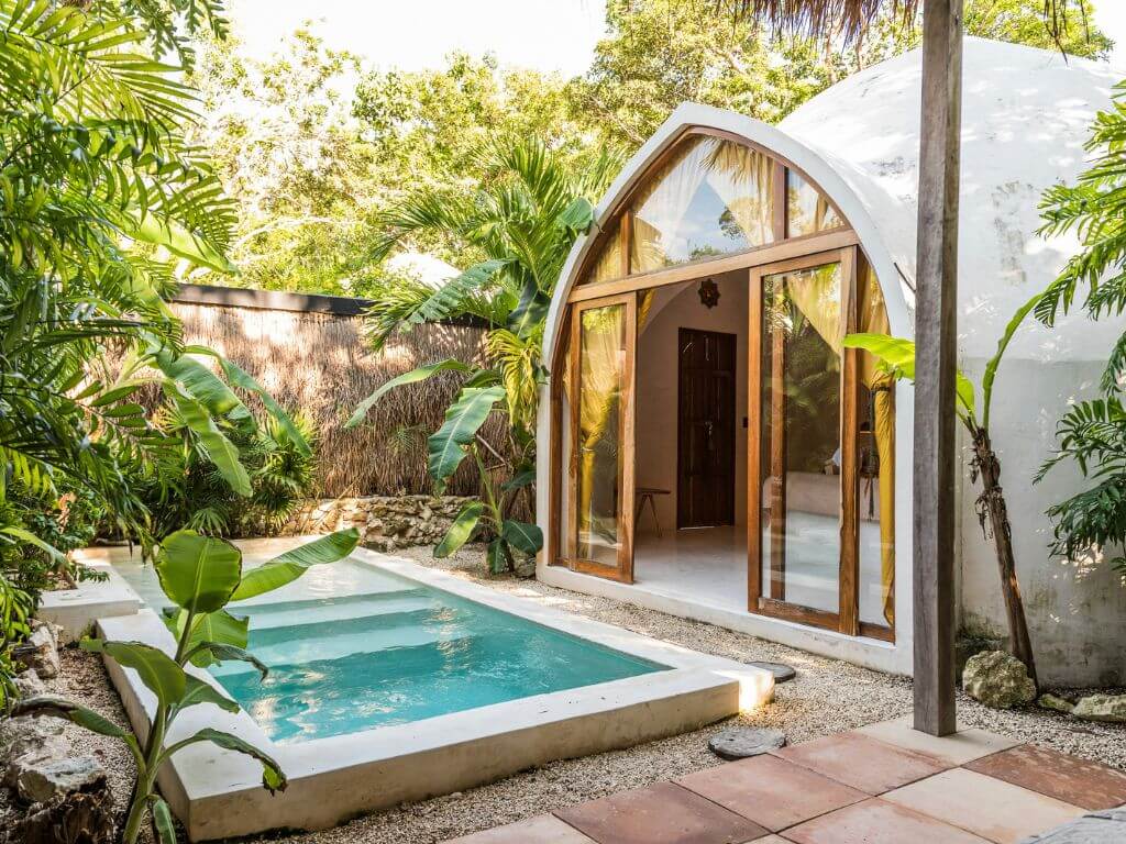 a dome shaped concrete villa opens onto a plant-filled courtyard with a turquoise pool in tulum