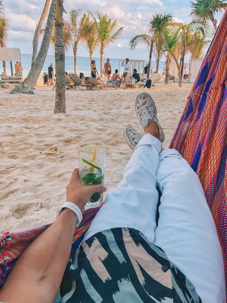 man lounging in hammock at a beach club in tulum