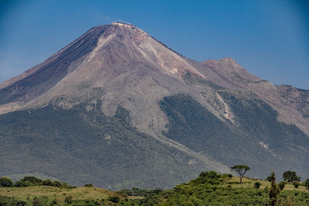 View of the towering Volcan de Colima with a tiny bit of green countryside in the foreground