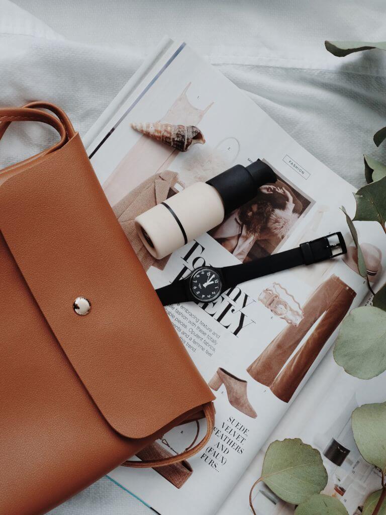 flat lay of leather purse and toiletries overtop of a beauty magazine