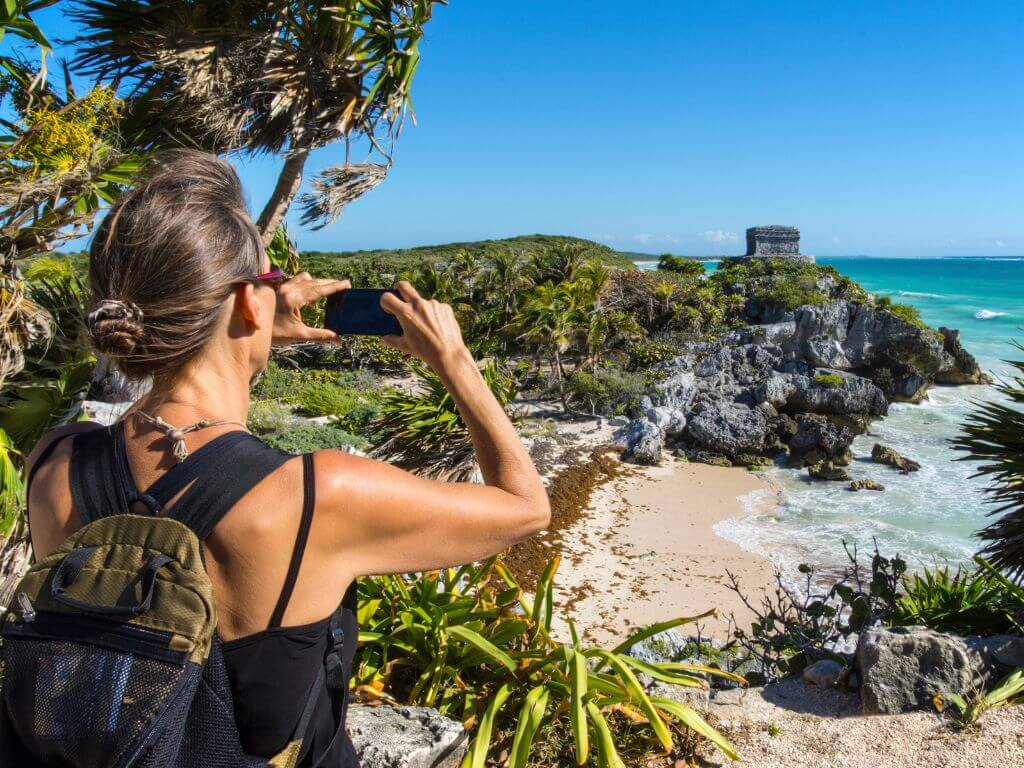 a woman snaps a photo of the tulum ruins on her smartphone